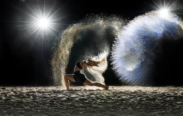 Девушка в черном костюме танцует на песке 