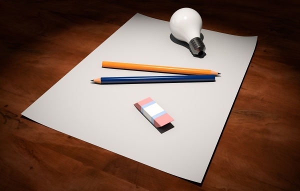 Лист бумаги, карандаши, ластик и лампочка на столе