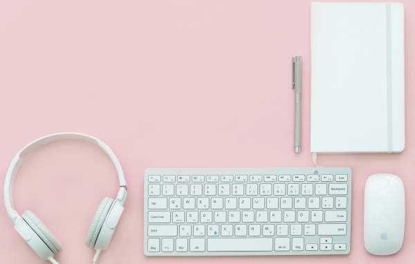 Наушники, клавиатура, блокнот с ручкой и мышка на розовом фоне
