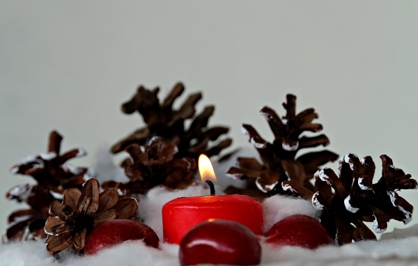 Красная зажженная свеча с шишками на сером фоне