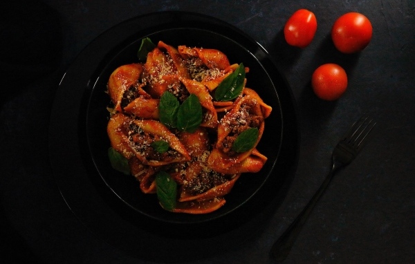 Большие макароны с фаршем в черной тарелке