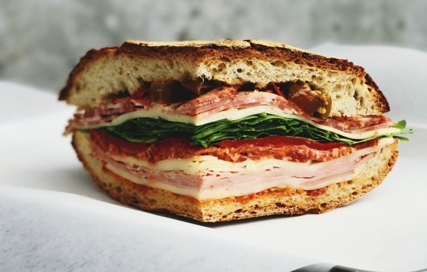 Кусок булки с колбасой, ветчиной и листьями салата