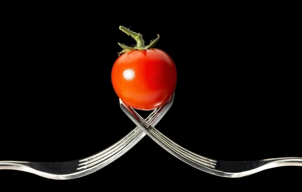 Красный помидор с вилками на черном фоне