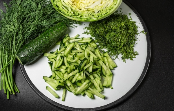 Нарезанные огурцы на столе с капустой и укропом