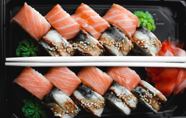 Суши с рыбой на черной тарелке с палочками