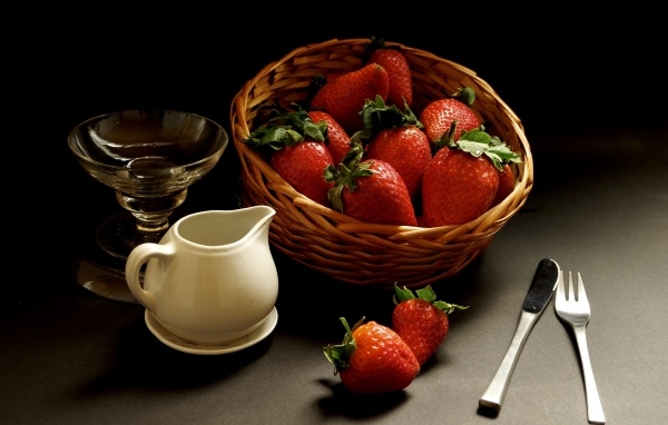 Корзина со спелой красной клубникой на столе с посудой