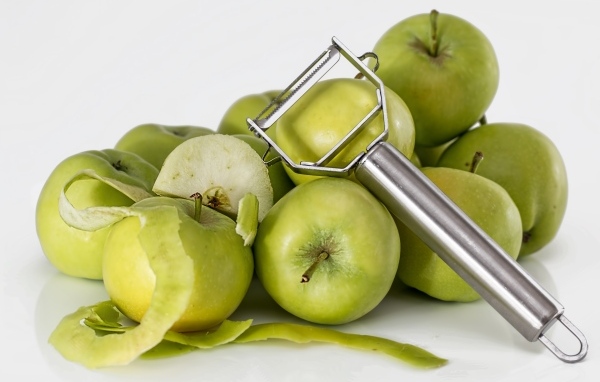 Зеленые яблоки с овощечисткой на белом фоне