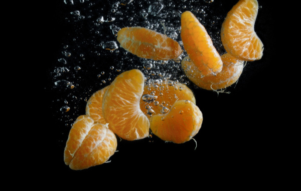 Дольки мандарина в воде на черном фоне