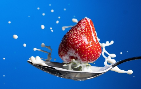 Молоко в ложке с клубникой на синем фоне