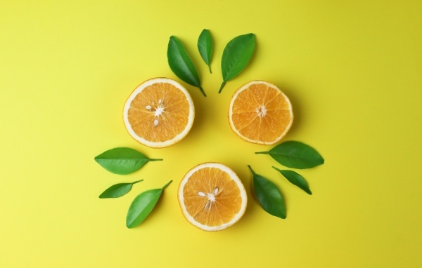 Половинки апельсина с зелеными листьями на желтом фоне