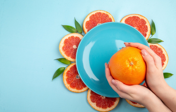 Апельсин в руках девушки на голубом фоне с тарелкой