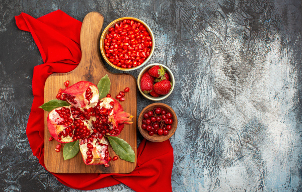 Очищенный гранат на столе с клубникой и ягодами смородины