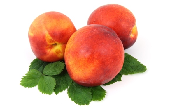 Три спелых персика с листьями на белом фоне