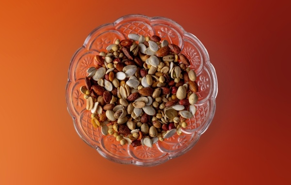 Разные орехи в стеклянной посуде на оранжевом фоне