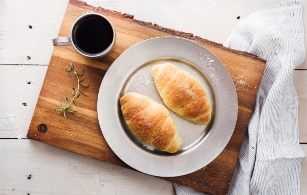 Два круассана на тарелке с чашкой кофе