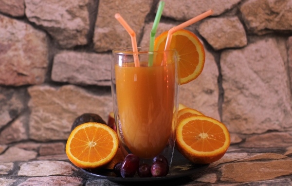 Стакан свежего сока с трубочками на столе с апельсинами