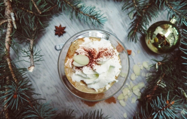 Горячий кофе с взбитыми сливками в чашке на столе с еловыми ветками