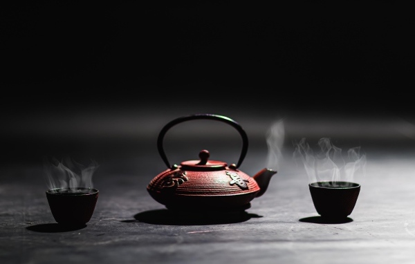 Чайник с горячим чаем на черном фоне