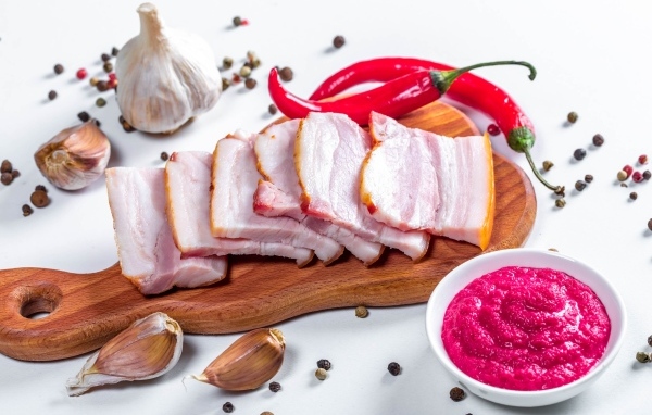 Нарезанное сало на столе с чесноком, хреном и красным перцем