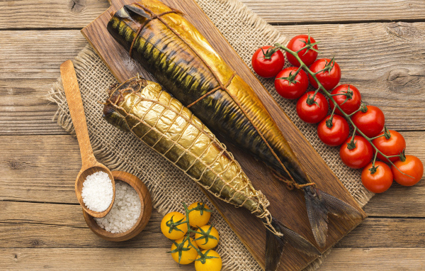 Две копченые скумбрии на столе с помидорами