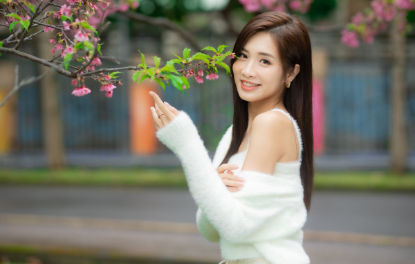 Красивая азиатка в белом свитере стоит у ветки дерева