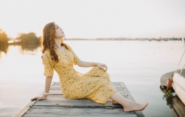 Красивая девушка в платье сидит на мосту у реки