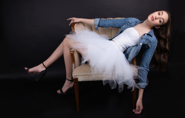 Девушка в белой юбке лежит в кресле на черном фоне