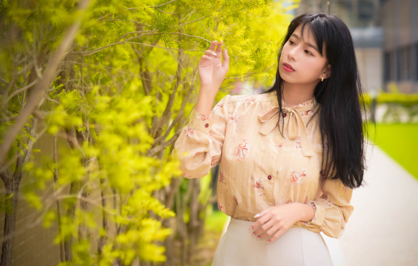 Молодая девушка азиатка стоит у дерева с зелеными листьями