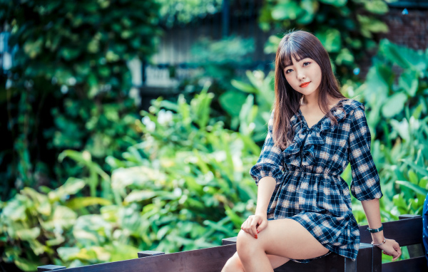 Молодая девушка в клетчатом платье сидит на заборе