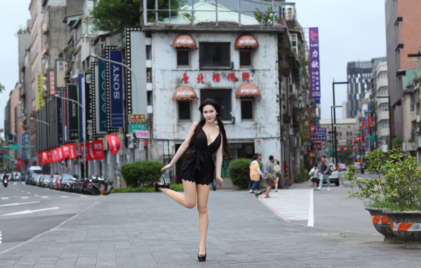 Девушка азиатка в черном платье стоит у дома