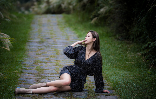 Девушка азиатка в платье лежит на дороге в парке