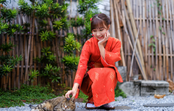 Девушка азиатка в красном платье гладит кота