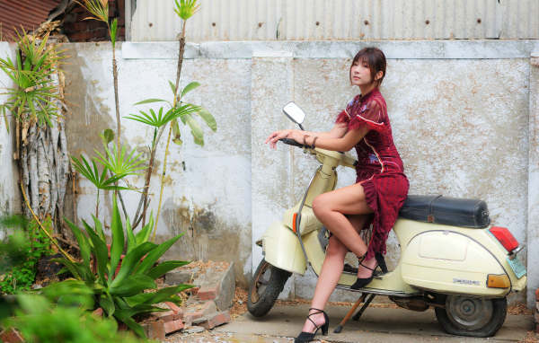 Девушка азиатка сидит на скутере у стены