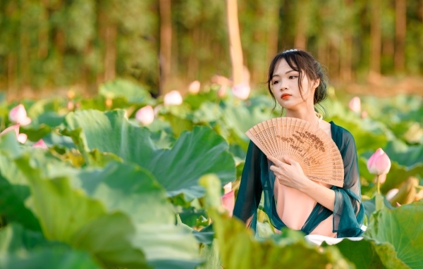 Девушка азиатка с веером в зеленых листьях лотоса