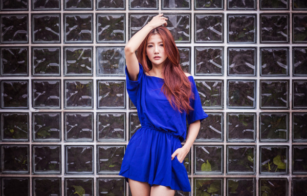 Азиатка в синем платье стоит у стеклянной стены