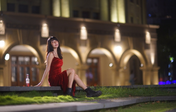 Азиатка в длинном красном платье сидит на ступенях