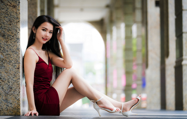 Азиатка в красном платье сидит у стены 
