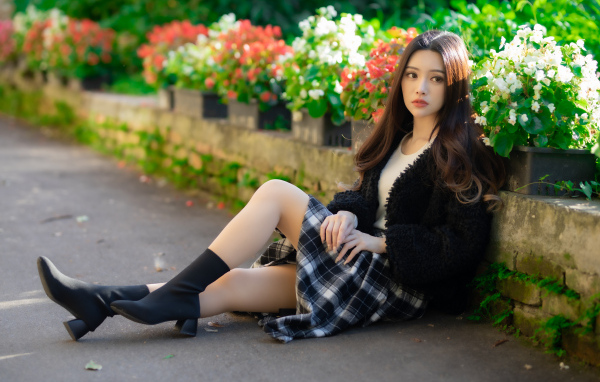 Азиатка сидит на асфальте у цветов