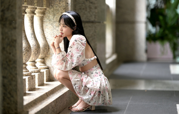 Красивая девушка азиатка в костюме сидит у стены