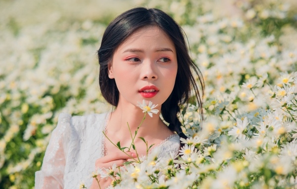 Красивая девушка азиатка на поле с белыми ромашками