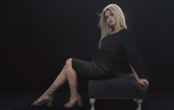 Красивая девушка в черном платье сидит на кресле
