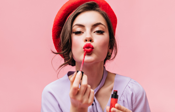Красивая девушка в красном берете красит губы