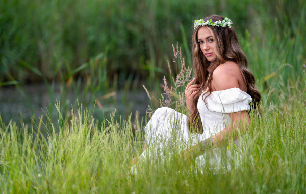 Красивая девушка в белом платье с венком на голове у пруда 