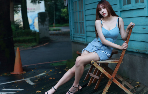 Красивая девушка сидит на стуле у дома