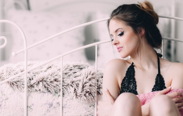 Красивая девушка сидит на полу у кровати 