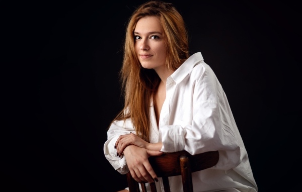 Милая девушка в белой рубашке сидит на стуле