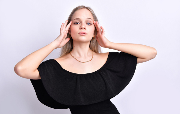 Девушка в черном платье с руками у головы на белом фоне