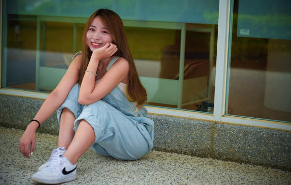 Девушка в джинсовом комбинезоне сидит на полу