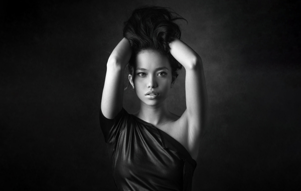 Девушка модель с руками в волосах  у стены