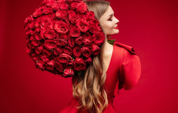 Девушка с большим букетом красных роз на красном фоне